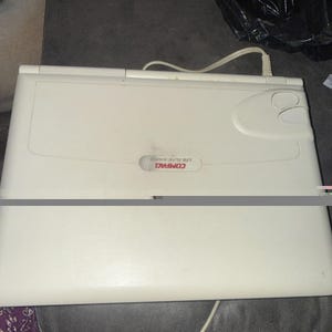 May include: A vintage off-white Compaq LTE Elite 4/40CX laptop computer with a closed lid. The device features a rectangular chassis, a central brand logo, and a power cable extending from the rear hinge area of the portable computing unit.