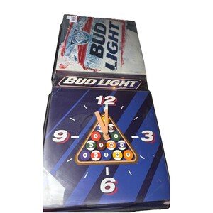 May include: A square clock with a blue face featuring a pool ball rack and the numbers 3, 6, 9, and 12. The clock has the Bud Light logo and a Bud Light beer can design on top.