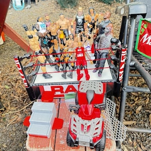 May include: A wrestling ring set with multiple action figures, a red and gray ATV, and a gray and red staircase. The wrestling ring has red ropes and the word "RAW" on the side.