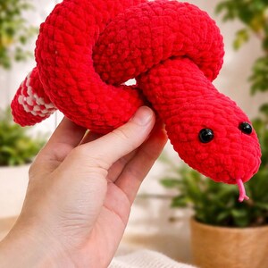 Peut inclure: Un jouet serpent en crochet rouge fait à la main, avec des yeux noirs et une langue rose. Le serpent est noué au milieu et a une queue rayée blanche et rouge. La peluche est douce et câline.