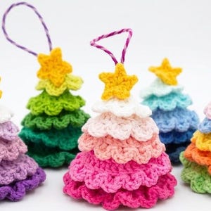 Op de afbeelding: Een verzameling van vijf kleine, kegelvormige gehaakte ornamenten in diverse kleuren. Elk ornament heeft gelaagde, geplooide lagen en is bekroond met een kleine gele ster. Drie ornamenten zijn voorzien van paars-witte gestreepte ophanglussen.