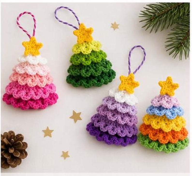 Op de afbeelding: Vier gehaakte kerstboomhangers met gele sterren als piek en paars-witte ophangkoorden. De boompjes hebben gelaagde, geschulpte texturen in diverse kleuren, waaronder roze, groen, paars, blauw, geel en oranje tinten.