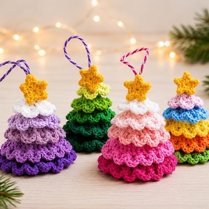 Può includere: Quattro decorazioni all'uncinetto fatte a mano a forma di alberi di Natale a strati. Ogni albero ha una stella gialla in cima e un cordino per appenderlo. Gli alberi sono viola, verdi, rosa e arcobaleno, tutti con bordi smerlati.