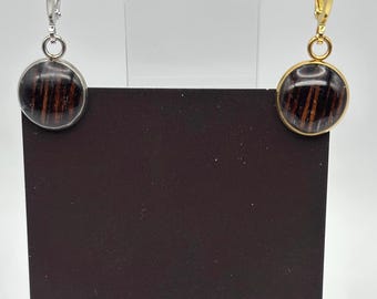 Puede incluir: Pendientes redondos con un diseño de veta de madera oscura, engarzados en plata y oro. Los pendientes se exhiben en una tarjeta negra con el texto blanco "MIDNIGHT TIMBER CO." y un logotipo de luna creciente y árbol.