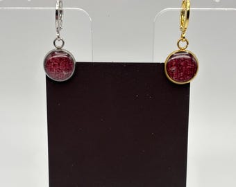Puede incluir: Un par de pendientes redondos con un diseño rojo y marrón. Uno tiene un aro plateado y el otro un aro dorado. Se exhiben en una tarjeta negra con el texto "MIDNIGHT TIMBER CO."