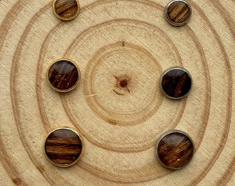 Puede incluir: Seis pendientes de madera con un patrón de vetas naturales están dispuestos sobre una rodaja de madera. Los pendientes tienen engastes de metal dorado y plateado. La veta de la madera es una mezcla de marrón y beige.