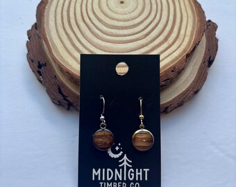 Puede incluir: Pendientes redondos de madera con ganchos plateados sobre una tarjeta negra, texto "MIDNIGHT TIMBER CO.". Los pendientes se presentan sobre un fondo de rodaja de madera. Diámetro de los pendientes: aproximadamente 1,5 cm.