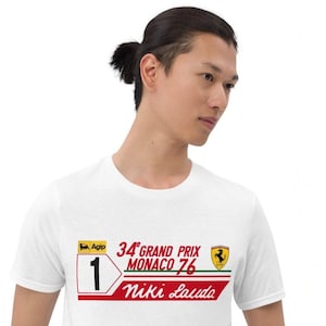 May include: White t-shirt with a graphic design celebrating the 1976 Monaco Grand Prix and Niki Lauda. The design includes the number 1, the words "34th Grand Prix Monaco 76", and the name "Niki Lauda" in red and white.