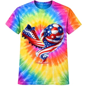 Puede incluir: Una camiseta de manga corta con un vibrante patrón tie-dye de arcoíris. El gráfico central muestra una bota de fútbol y un balón de fútbol, ambos decorados con el motivo de la bandera estadounidense en rojo, blanco y azul, unidos por una estela patriótica.