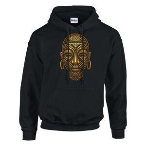 Può includere: Felpa con cappuccio nera con un disegno di maschera tribale dorata sul davanti. La maschera presenta intricati motivi geometrici e grandi orecchini a cerchio. La felpa ha una tasca frontale e un cappuccio con coulisse.