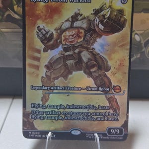 May include: A collectible trading card featuring "Krang, Utrom Warlord," a Legendary Artifact Creature. The card depicts a detailed illustration of a robot with a menacing face. The card is held in a clear plastic stand.