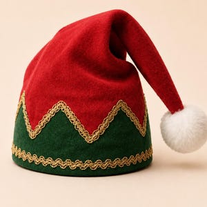 May include: A red and green felt hat featuring a zigzag pattern along the base. The hat is accented with gold metallic trim along the edges and a white pom-pom attached to the tip. The design is structured with a pointed, drooping top section.