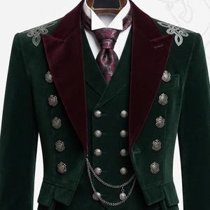 May include: A dark green velvet tailcoat suit featuring a double-breasted vest with silver buttons, a deep burgundy velvet lapel, and a matching patterned tie. The jacket includes silver shoulder embroidery and a decorative silver chain across the vest.