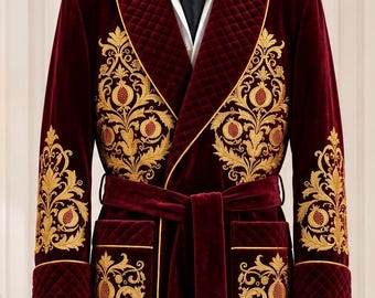 May include: A floor-length burgundy velvet smoking robe featuring gold embroidered pomegranate motifs on the chest and sleeves. The robe includes a quilted shawl collar, matching tie belt with gold tassels, and two front pockets with gold piping.