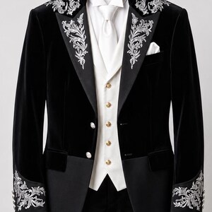 May include: A black velvet tailcoat featuring silver floral embroidery on the lapels and cuffs, paired with a white vest with gold buttons, a white dress shirt, a white necktie, and a white pocket square, all displayed on a wooden hanger.