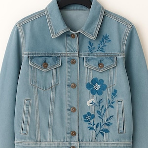 以下が含まれることがあります： ブルーデニムジャケット、ブルーと白の花柄刺繍入り。 ジャケットはクラシックな襟、ボタン留め、2つの胸ポケット、2つのサイドポケット付き。 黒いハンガーにかかっています。