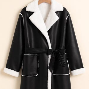 May include: A long black coat with a white faux fur collar, cuffs, and lining. The coat has a matching black belt and white trim around the pockets and edges. The coat is hanging on a wooden hanger.