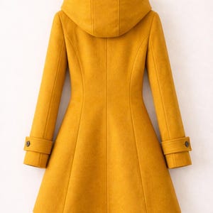 May include: A mustard yellow coat with a hood, long sleeves, and a flared hemline. The coat features a structured back panel design with vertical seams and cuffs on each sleeve, each accented with a single dark button detail for a finished look.