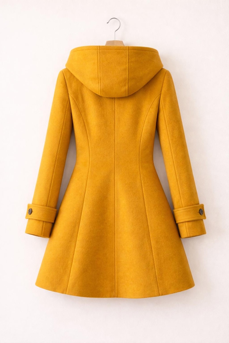 May include: A mustard yellow coat with a hood, long sleeves, and a flared hemline. The coat features a structured back panel design with vertical seams and cuffs on each sleeve, each accented with a single dark button detail for a finished look.
