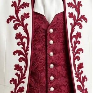 May include: A white jacket featuring deep red floral embroidery along the lapels, worn over a dark red paisley vest with six white buttons. A white cravat is secured at the neck with a silver-toned brooch featuring a central white stone.