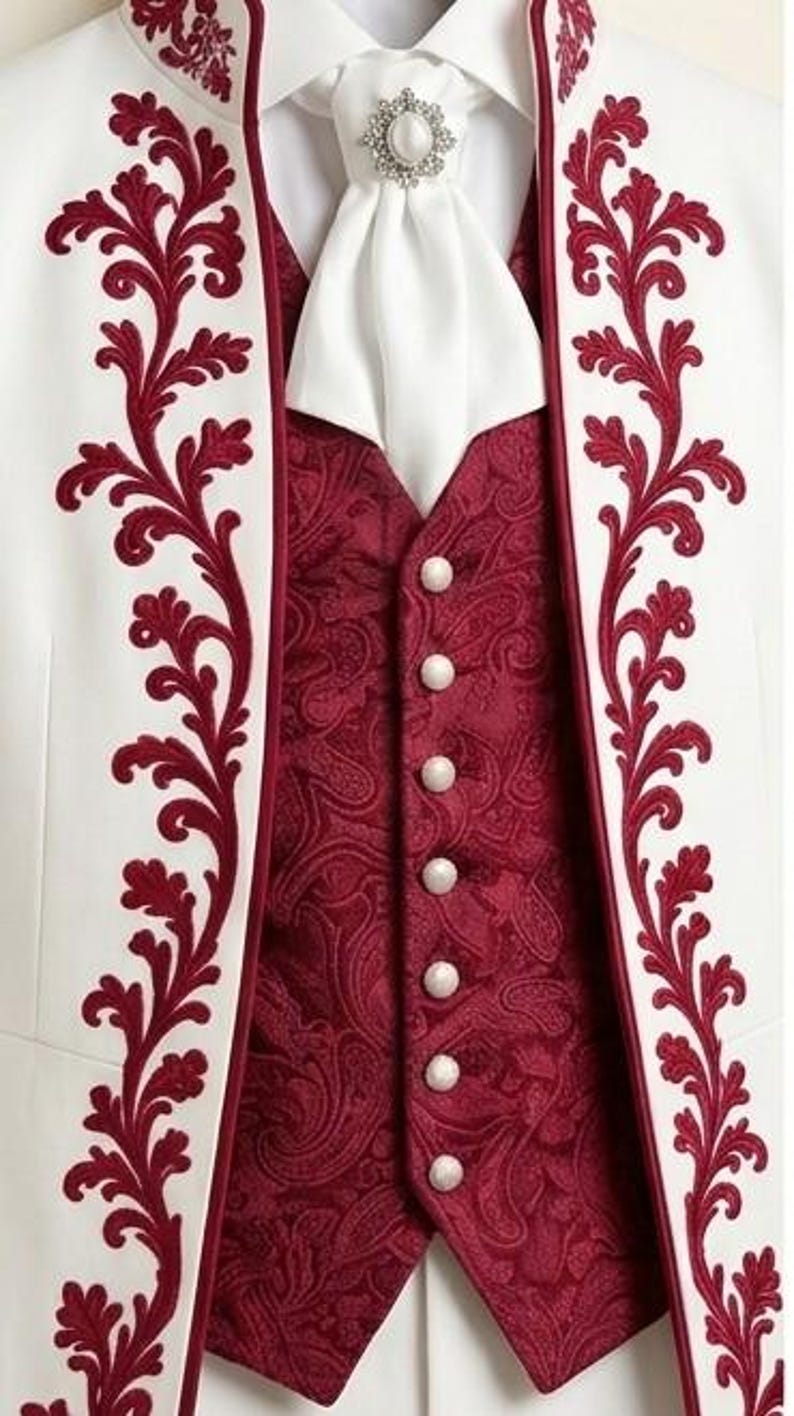 May include: A white jacket featuring deep red floral embroidery along the lapels, worn over a dark red paisley vest with six white buttons. A white cravat is secured at the neck with a silver-toned brooch featuring a central white stone.