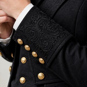 May include: A black jacket featuring intricate tonal floral embroidery on the cuffs and lapels. The garment is adorned with multiple polished gold-tone metal buttons arranged in rows along the sleeve cuffs and the front closure.