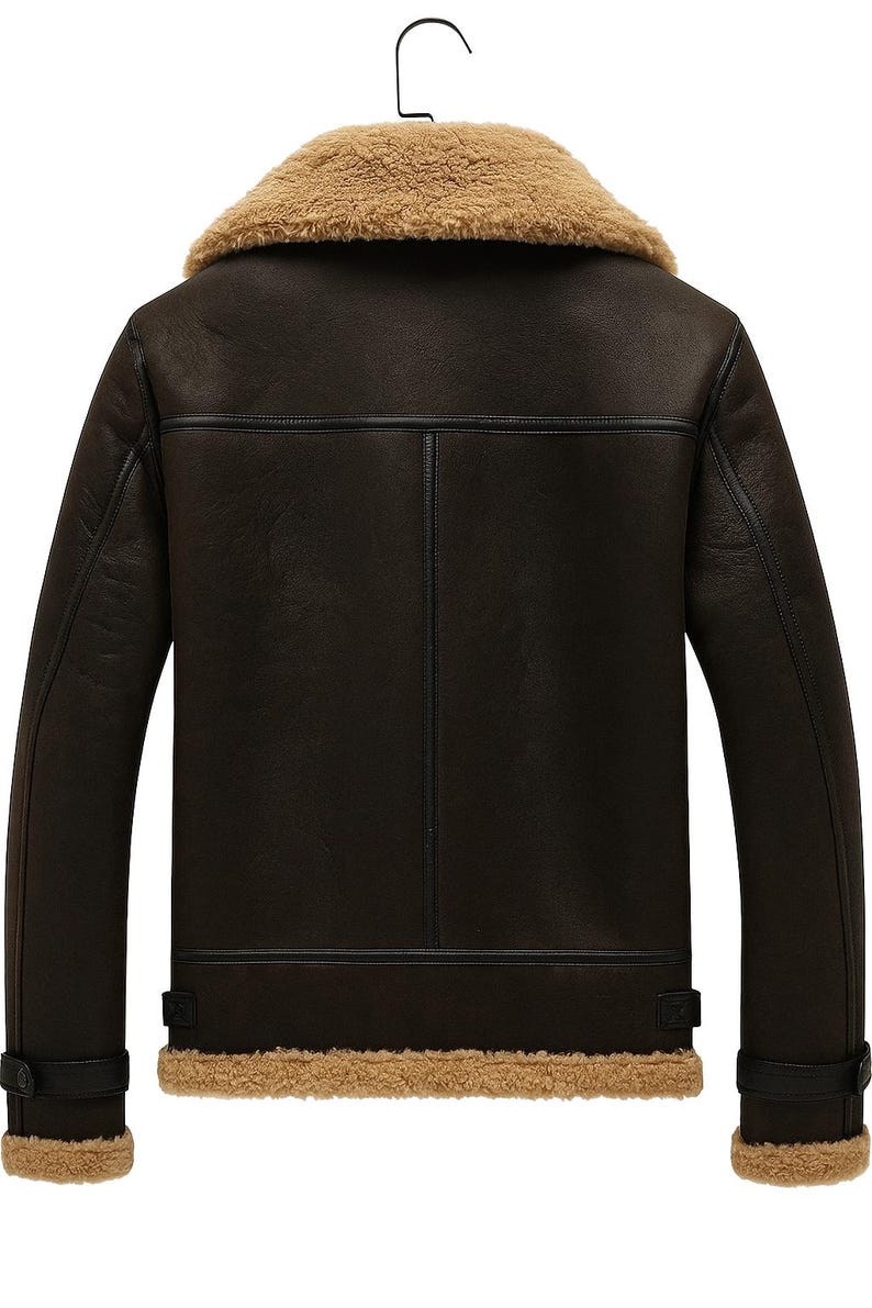 May include: A brown leather jacket with a tan shearling collar and lining. The jacket has a classic design with a button closure at the cuffs and a vertical seam detail on the back. The jacket is hanging on a black hanger.