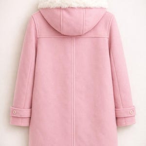 May include: A light pink duffel coat with a hood and white faux fur trim. The coat has a button closure and two buttons on the sleeves. The coat is hanging on a wooden hanger.