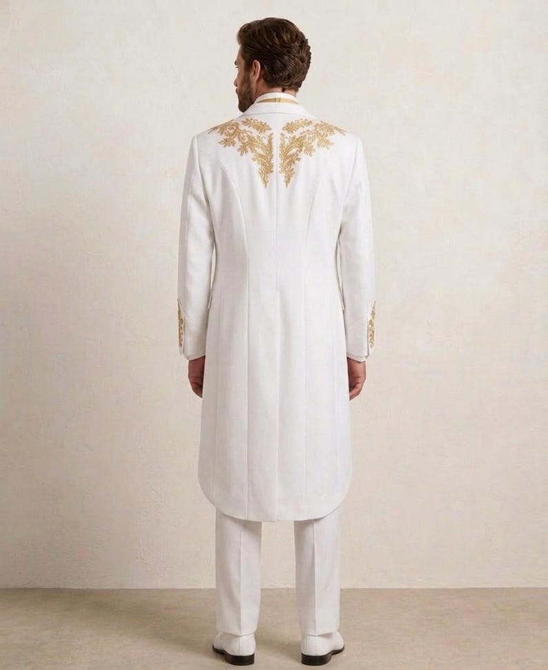 May include: A long white coat featuring intricate gold embroidery across the upper back and shoulders, paired with matching white trousers and white shoes. The coat has a structured collar, long sleeves with gold detailing at the cuffs, and a hem.