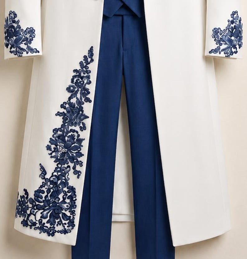 May include: A white long coat featuring intricate dark blue floral embroidery along the front panel and cuffs, paired with solid dark blue trousers. The coat has a structured open front design, while the trousers feature a clean, tailored finish.