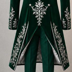 Puede incluir: Una levita de terciopelo verde oscuro con intrincados bordados plateados en los paneles frontales y pu&ntilde;os, combinada con pantalones verde oscuro a juego. La chaqueta incluye botones plateados y un forro claro visible en el dobladillo.