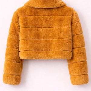May include: Mustard-colored faux fur jacket with a collar and horizontal stripe design. The cropped jacket is hanging on a white background. The jacket has long sleeves.