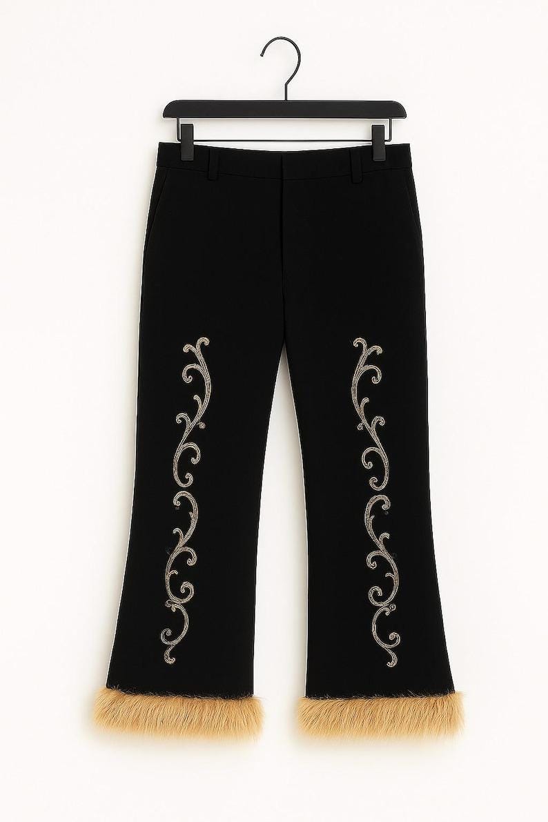 Puede incluir: Pantalones negros con un patr&oacute;n de volutas plateadas bordadas verticalmente en cada pierna y un borde de piel sint&eacute;tica color canela en el dobladillo inferior. Los pantalones se muestran en una percha negra, con corte recto.