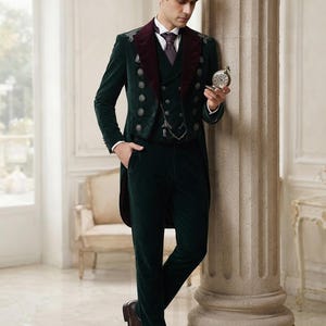 May include: A dark green velvet tailcoat suit featuring a deep burgundy velvet lapel, a matching waistcoat with silver-toned buttons, and dark green velvet trousers. The ensemble includes a white collared shirt, a dark tie, and brown leather shoes.
