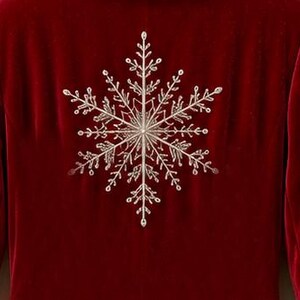 May include: A deep red velvet blazer featuring large, intricate silver embroidered snowflake patterns centered on the back and extending across the sleeves. The embroidery consists of fine, detailed lines forming a classic six-pointed star design.