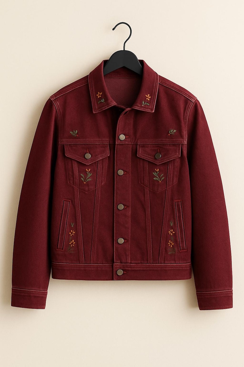 May include: A burgundy denim jacket with floral embroidery. The jacket has a classic collar, button-down front, two chest pockets, and two side pockets. The floral embroidery is in shades of green, yellow, and orange.