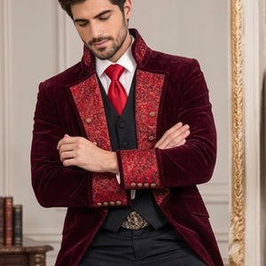 Puede incluir: Una levita de terciopelo color burdeos intenso con solapas y pu&ntilde;os estampados de cachemira en rojo y negro, adornada con botones dorados. Se lleva sobre un chaleco negro, una camisa blanca de cuello r&iacute;gido y una corbata roja, con pantalones negros.