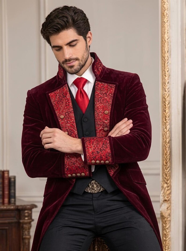 Puede incluir: Una levita de terciopelo color burdeos intenso con solapas y pu&ntilde;os estampados de cachemira en rojo y negro, adornada con botones dorados. Se lleva sobre un chaleco negro, una camisa blanca de cuello r&iacute;gido y una corbata roja, con pantalones negros.