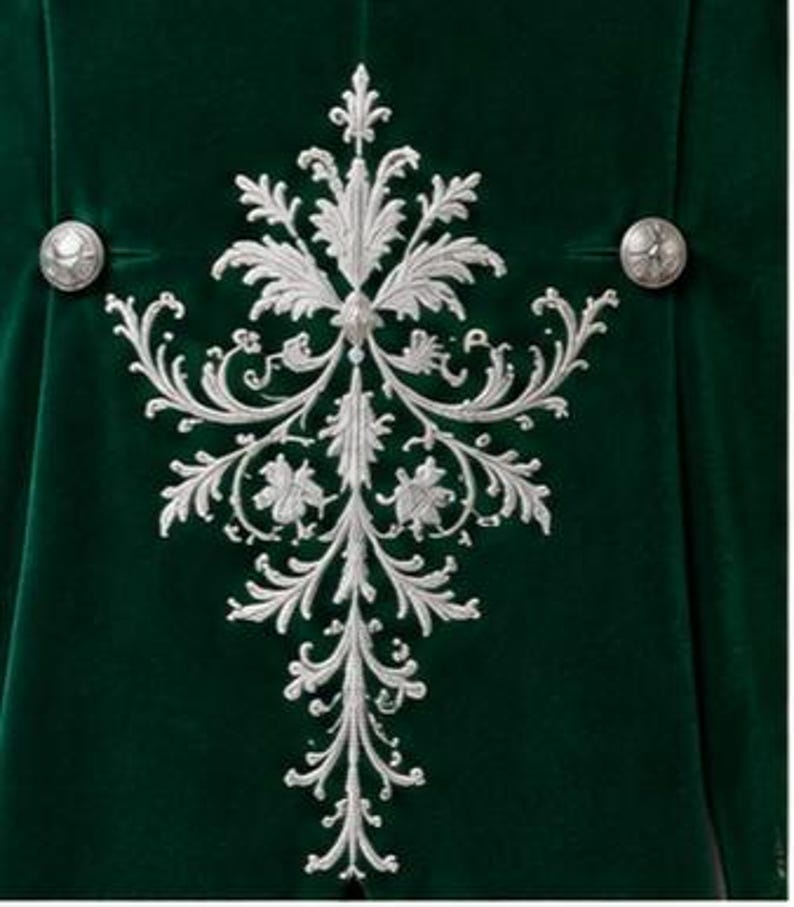 Puede incluir: Una prenda de terciopelo verde intenso con un gran patr&oacute;n de bordado plateado intrincado en el centro. El dise&ntilde;o consta de motivos florales y de hojas sim&eacute;tricos y en espiral. Se aprecian dos botones redondos de metal plateado.