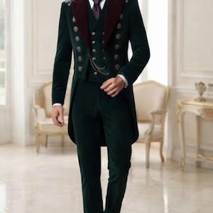 May include: A dark green velvet tailcoat suit featuring a deep burgundy lapel, a matching waistcoat with two columns of silver buttons, a white collared shirt, and a purple necktie. The jacket includes silver shoulder embroidery and a chain detail.