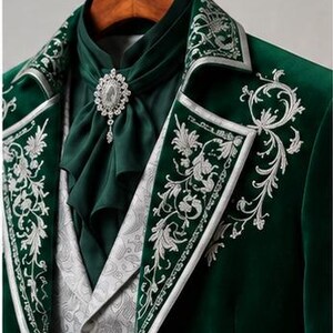 Puede incluir: Un blazer de terciopelo verde oscuro con intrincados bordados plateados en las solapas y el pecho. La prenda se combina con un corbat&oacute;n verde oscuro a juego sujeto por un broche ovalado de cristal y un chaleco gris claro con estampado paisley.