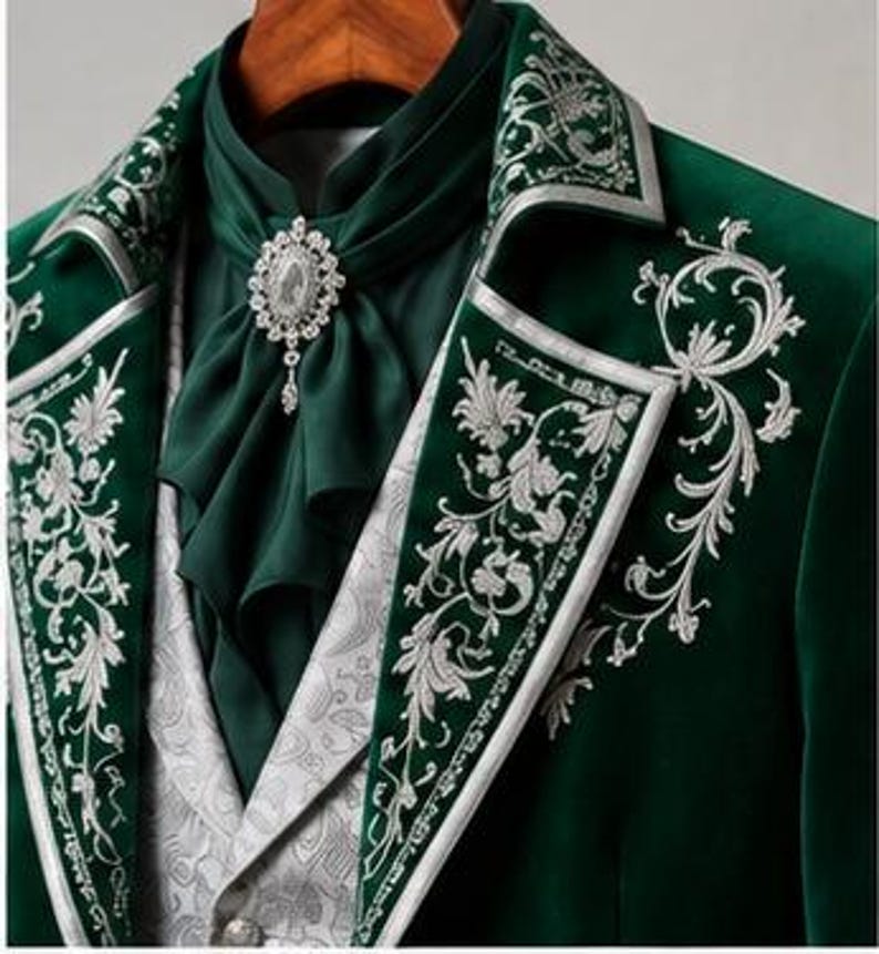 Puede incluir: Un blazer de terciopelo verde oscuro con intrincados bordados plateados en las solapas y el pecho. La prenda se combina con un corbat&oacute;n verde oscuro a juego sujeto por un broche ovalado de cristal y un chaleco gris claro con estampado paisley.