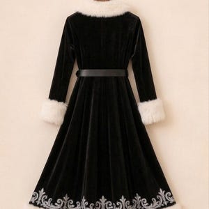 May include: A long-sleeved black velvet coat featuring a white faux fur collar and matching white faux fur cuffs. The coat includes a black belt at the waist and a silver embroidered floral pattern along the bottom hem, finished with a white faux fur trim.