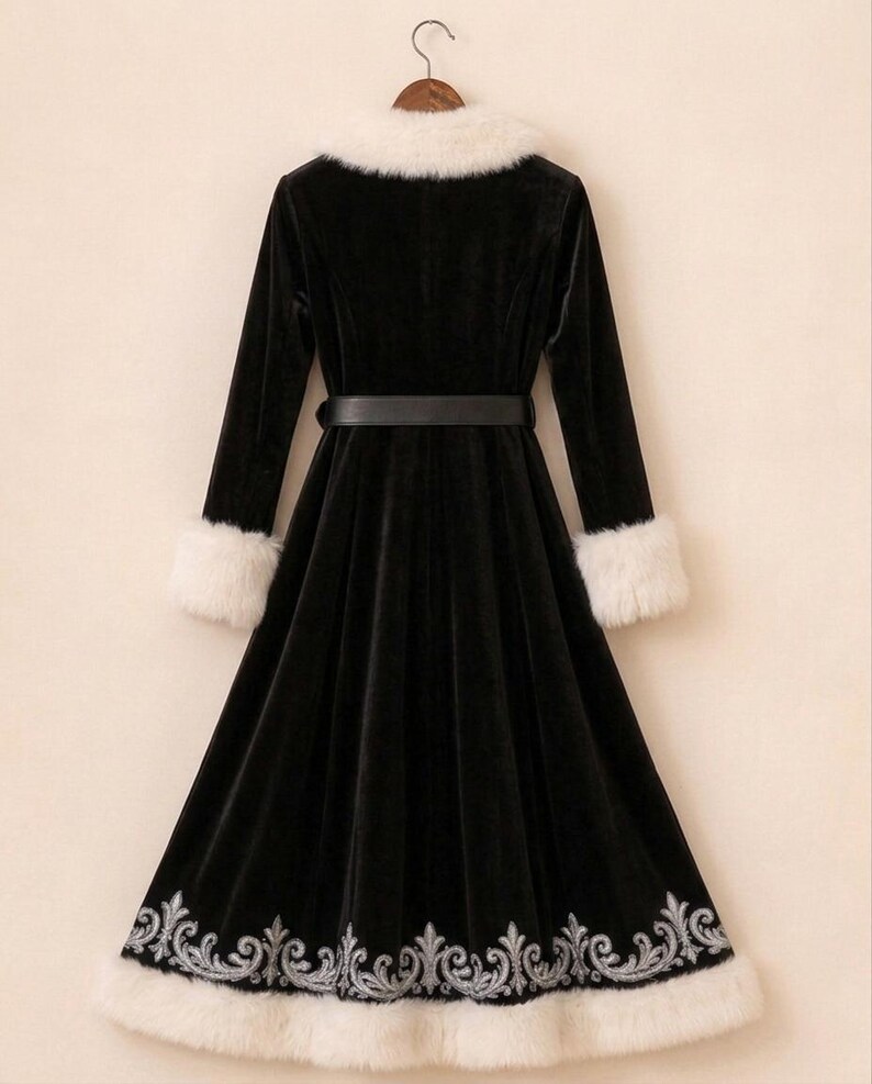 May include: A long-sleeved black velvet coat featuring a white faux fur collar and matching white faux fur cuffs. The coat includes a black belt at the waist and a silver embroidered floral pattern along the bottom hem, finished with a white faux fur trim.