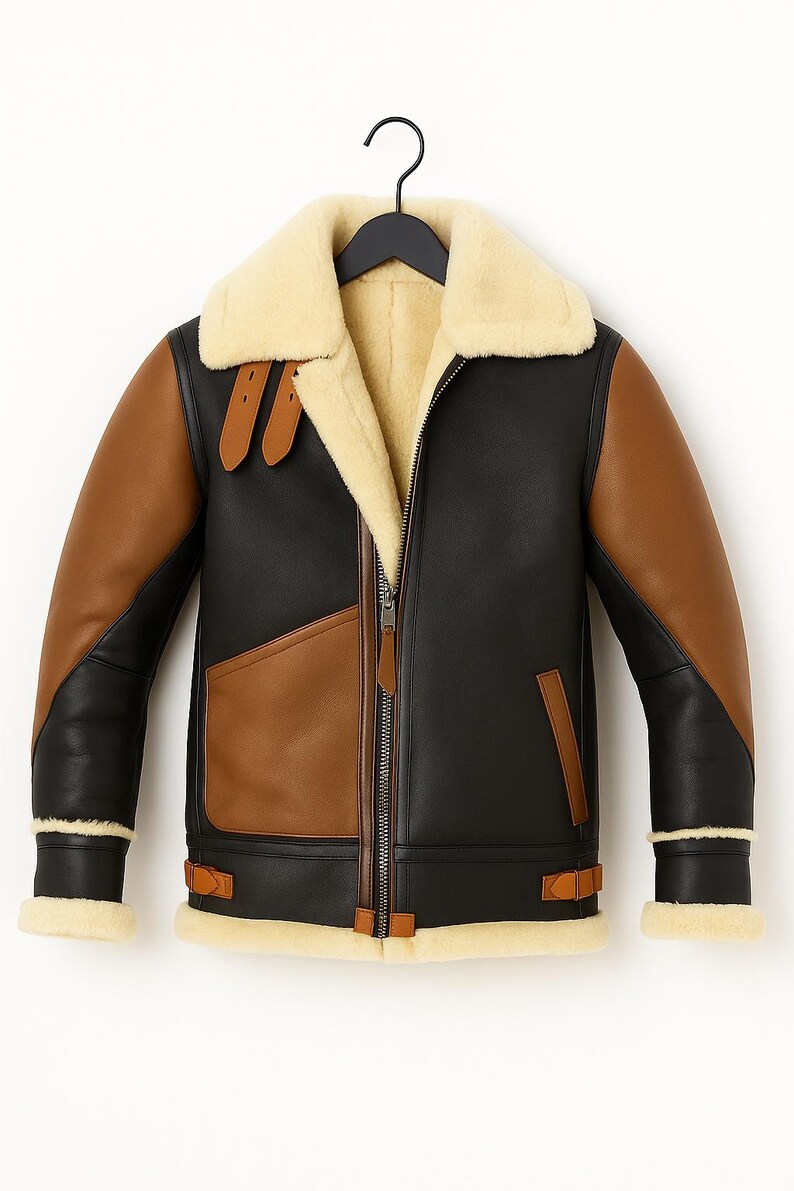 May include: A black and brown leather jacket with a cream-colored shearling collar and lining. The jacket features brown sleeves, a front zipper, and brown leather accents. It hangs on a black hanger.