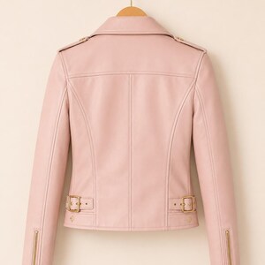 May include: A pale pink leather jacket in a classic biker style. It has a notched collar, shoulder epaulettes, and gold-tone hardware on the zips and buckles. The jacket is hanging on a wooden hanger.