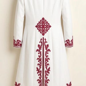 May include: A white long-length coat and matching trousers featuring deep red embroidery. The coat has a high collar, long sleeves, and a central back vent, all accented with intricate red floral patterns along the edges and hemline.