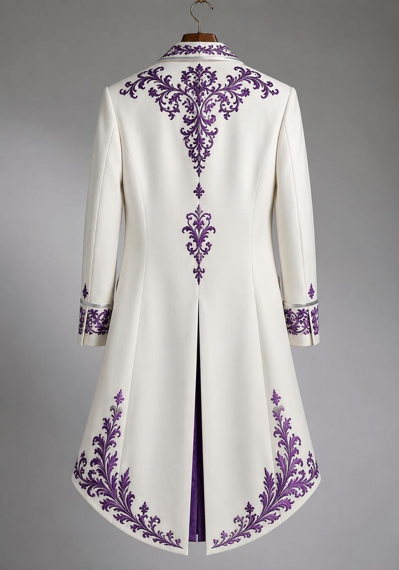 May include: A long white coat featuring intricate purple embroidery along the collar, back, cuffs, and hem. The garment has a structured silhouette with a center back vent, long sleeves, and a high collar, displayed on a wooden hanger.