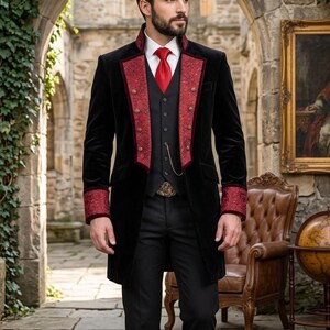 Puede incluir: Una levita de terciopelo negro con solapas y pu&ntilde;os de patr&oacute;n rojo con botones dorados, sobre un chaleco negro, camisa blanca de cuello y corbata roja. El conjunto incluye pantalones negros y una cadena de reloj de bolsillo dorada en el chaleco.