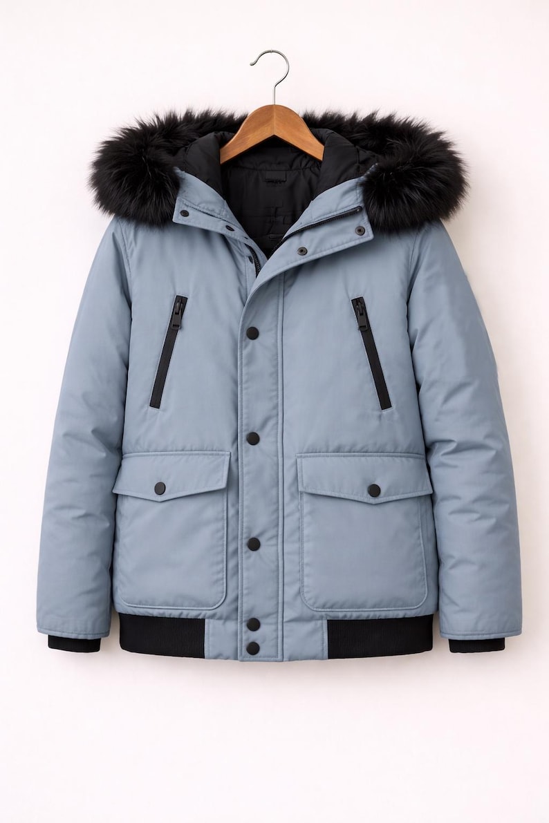 May include: A pale blue winter jacket with a black fur-trimmed hood. The jacket has a black lining, black zips, and black buttons. It features two front pockets and a black ribbed hem.